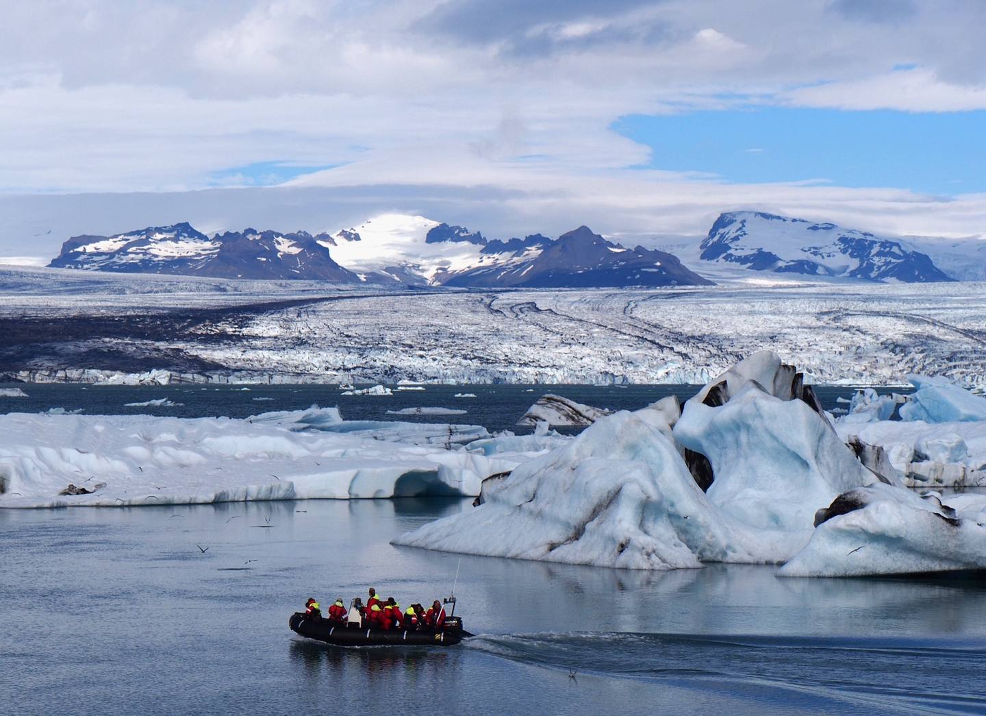 A Zodiac boat passing blue icebergs on Jökulsárlón with the glacier beyond